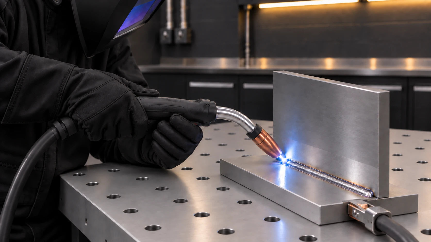 Welder supporting a MIG gun with two gloved hands at a steel joint